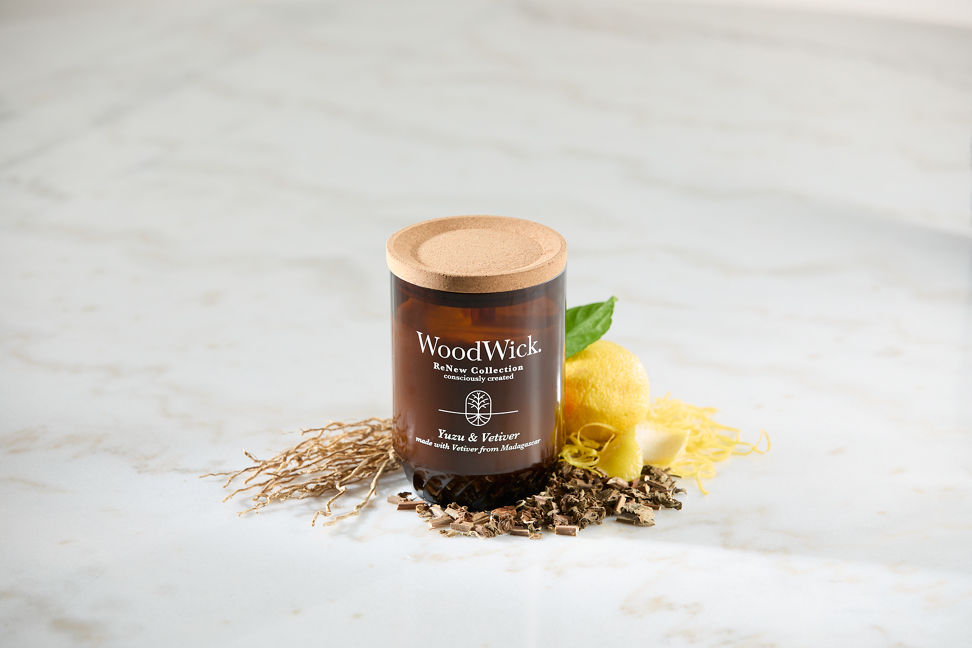 WoodWick ReNew Collection Yuzu & Vetiver Large Candle on a table surrounded by a lemon, shaved lemon peel, and dried plant pieces