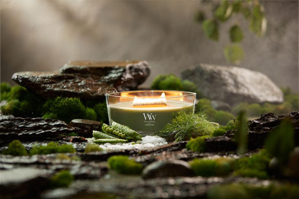 WoodWick Vapour Trails Collection Ethereal Haze Ellipse Candle surrounded by rocks, moss, salt, and snap peas