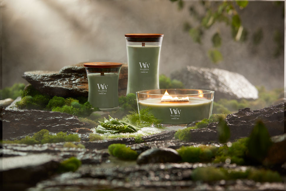 WoodWick Vapour Trails Collection Ethereal Haze Medium Hourglass Candle, Ethereal Haze Large Hourglass Candle, and Ethereal Haze Ellipse Candle surrounded by rocks, moss, salt, and snap peas in a forest setting