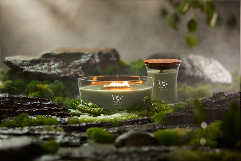 WoodWick Vapour Trails Collection Ethereal Haze Ellipse Candle and Ethereal Haze Medium Hourglass Candle surrounded by rocks, moss, salt, and snap peas in a forest setting
