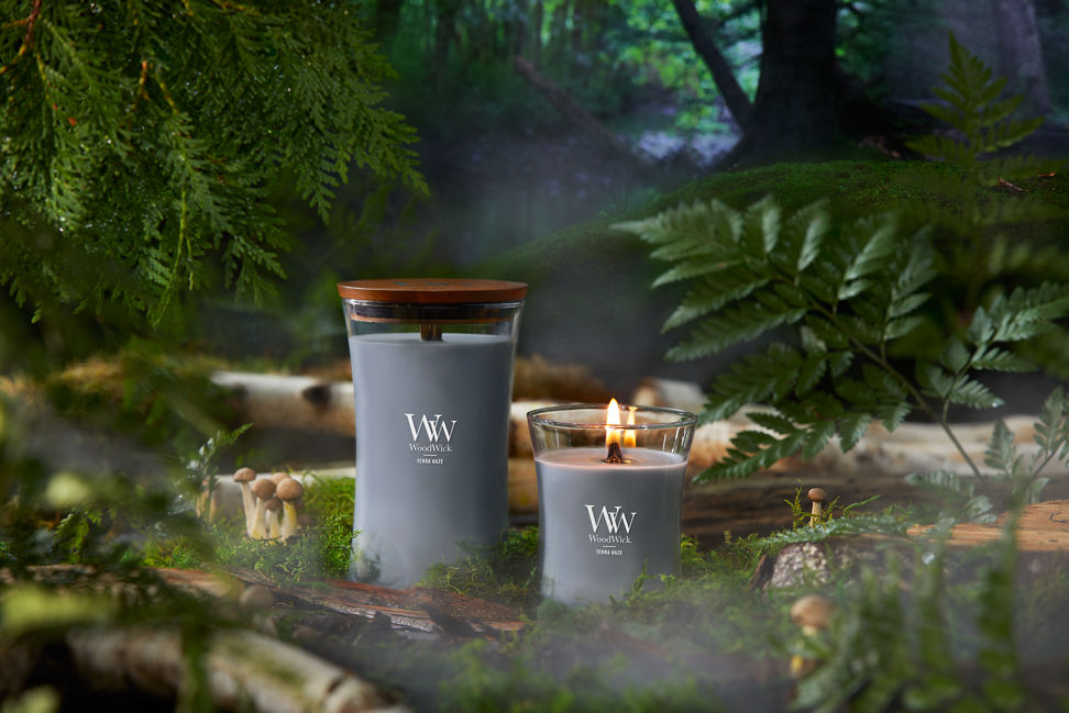 WoodWick Vapour Trails Collection Terra Haze Large Hourglass Candle and Terra Haze Medium Hourglass Candle surrounded by mushrooms, tree branches, moss, and leaves in a forest setting