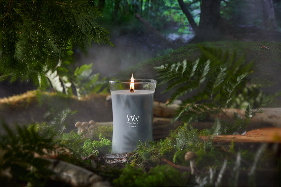 WoodWick Vapour Trails Collection Terra Haze Large Hourglass Candle in a forest setting surrounded by leaves, mushrooms, and trees