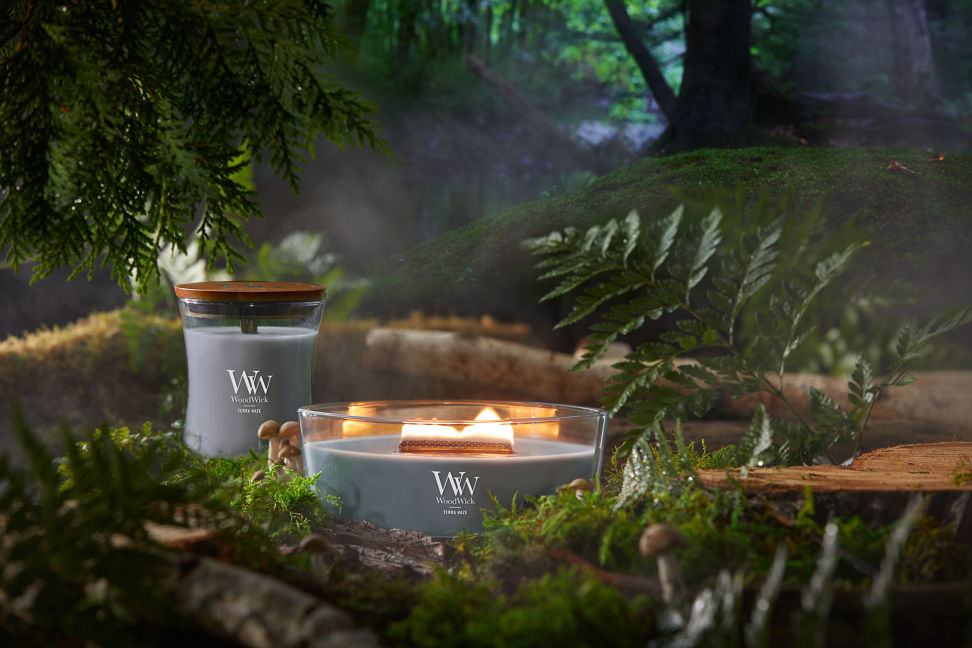 WoodWick Vapour Trails Collection Terra Haze Ellipse Candle and Terra Haze Large Hourglass Candle in a forest setting surrounded by trees, leaves, and mushrooms