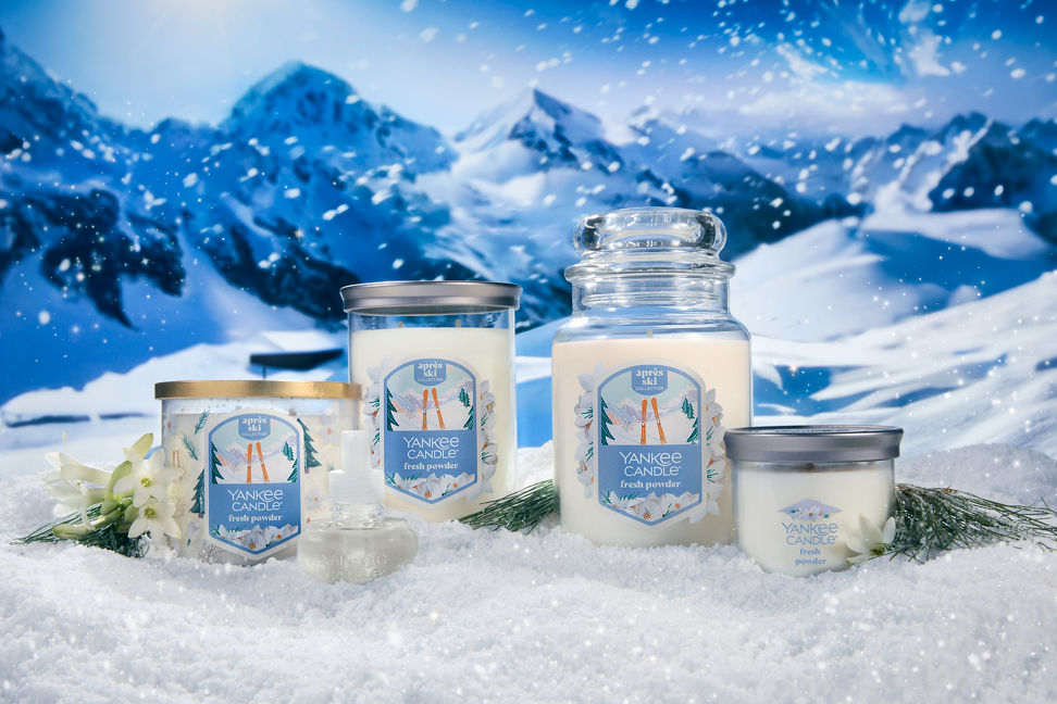 Apres Ski Collection Fresh Powder 3-Wick Candle, Fresh Powder ScentPlug Refill, Fresh Powder Signature Large Tumbler Candle, Fresh Powder Original Large Jar Candle, and Fresh Powder Signature Small Tumbler Candle surrounded by snow, flowers, and mountains
