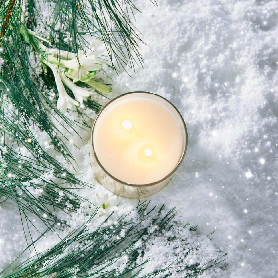 a Signature Large Tumbler Candle surrounded by snow, flowers, and branches