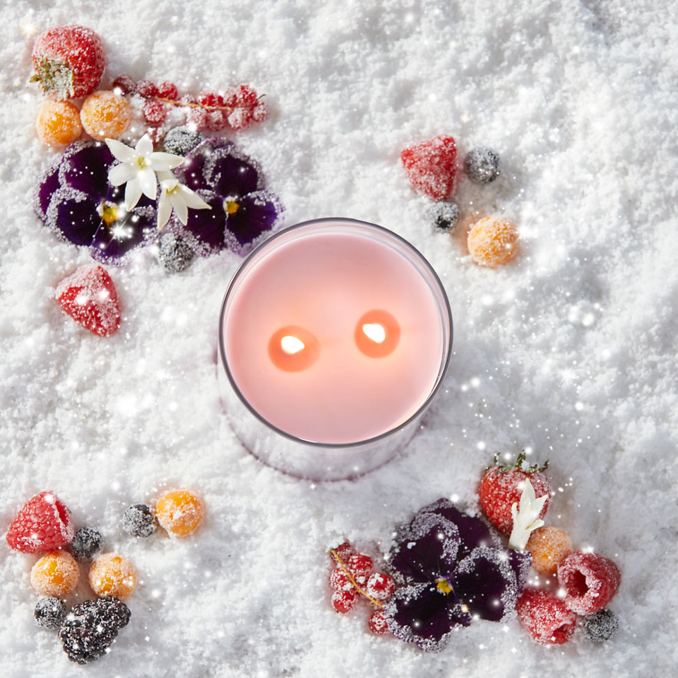 a pink-colored Signature Large Tumbler Candle in snow surrounded by berries