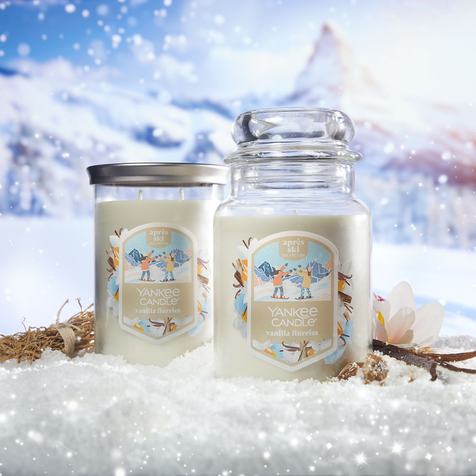 Apres Ski Collection Vanilla Flurries Signature Large Tumbler Candle and a Vanilla Flurries Original Large Jar Candle in snow surrounded by a flower, vanilla, and mountains
