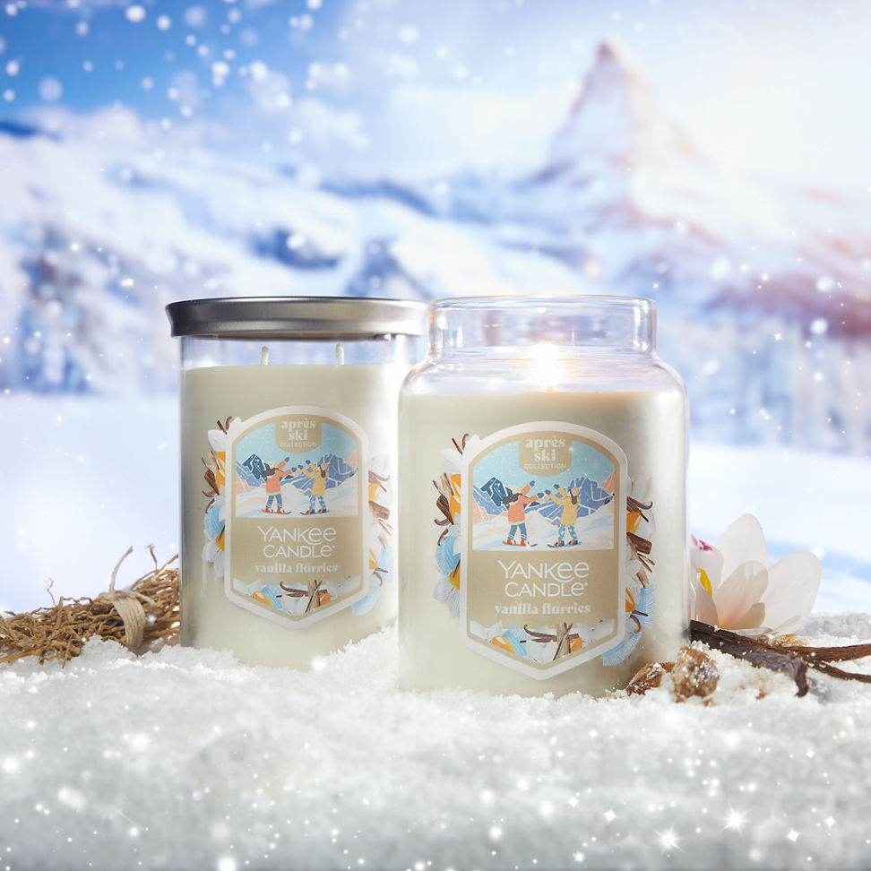 Apres Ski Collection Vanilla Flurries Signature Large Tumbler Candle and a Vanilla Flurries Original Large Jar Candle in snow surrounded by vanilla, a flower, and mountains