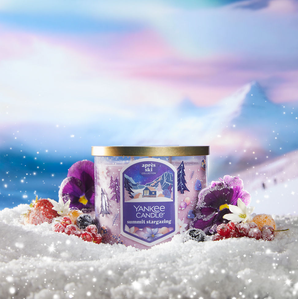 summit stargazing three wick candle on snowy surface with frosted flowers and berries and with mountains in distance