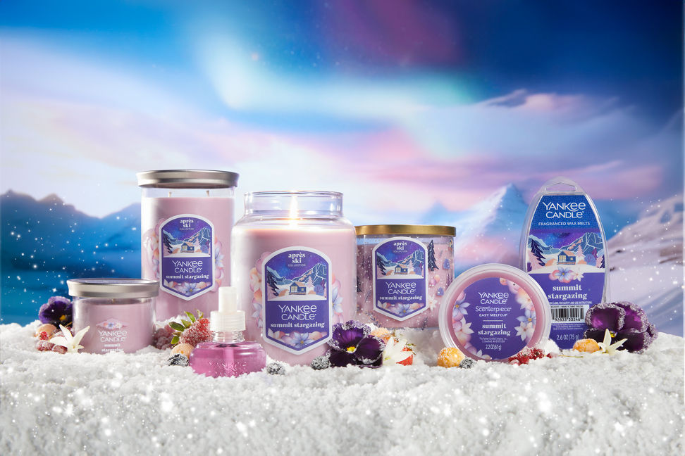 an array of summit stargazing products and candles on a snowy surface with flowers and berries and with mountains in distance