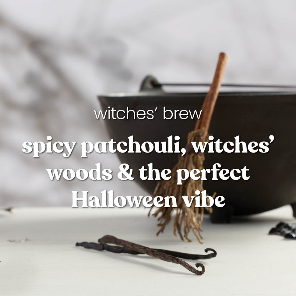 Large cauldron with rustic broom, Halloween decor, and text about spicy patchouli and witches’ woods fragrance.
