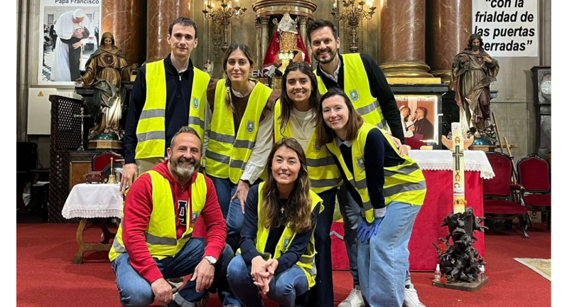 A group of seven individuals wearing yellow vests are inside a church, posing in front of a decorated altar, indicating their volunteer work in the community.
