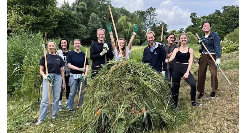A team of about eight people is shown in an outdoor setting, posing with tools used for clearing vegetation, demonstrating environmental conservation work.