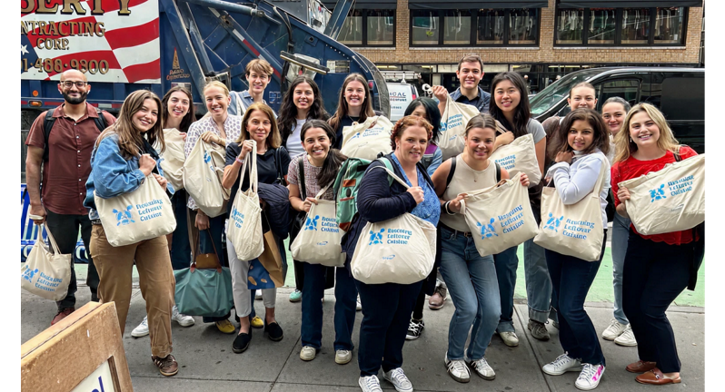 A group of approximately 16 individuals stands on a city street, holding canvas bags labeled "Rescuing Leftover Cuisine", in front of a garbage truck, showing participation in food rescue activities.