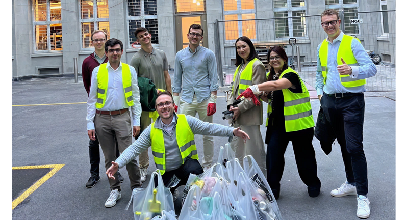 A group of eight people wearing bright yellow vests are gathered in a courtyard, posing with several garbage bags filled with waste, indicating teamwork in a community cleanup effort.