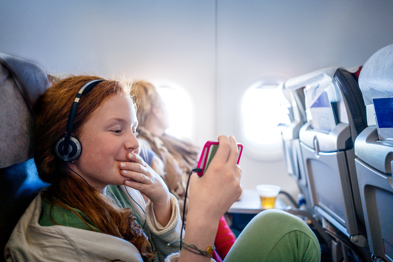 Girl sitting in an airplane passing time on her mobile phone watching a movie while waiting for landing. Small version