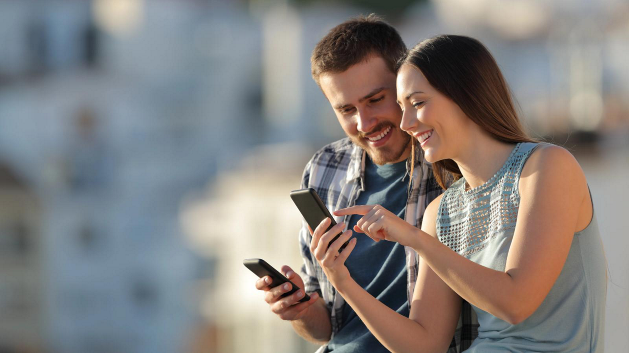 Happy couple sharing phone in a town