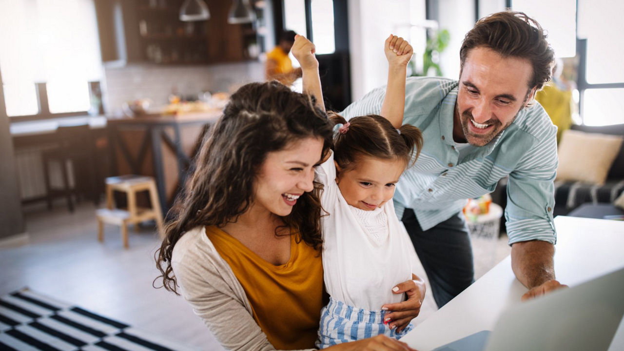Excited family sitting at a home office desk with their child, looking at a laptop smiling