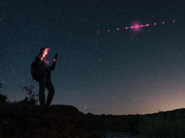 Person stargazing under night sky with light trail