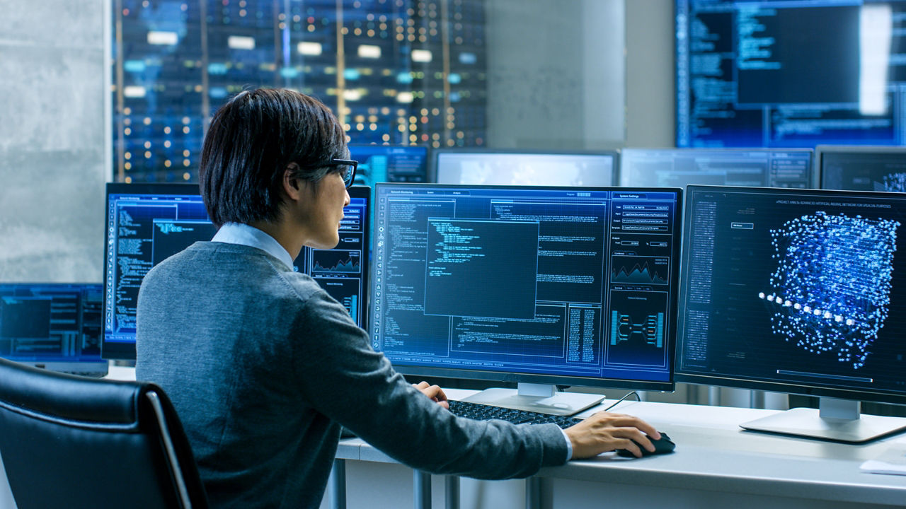 In the System Control Room Technical Operator Works at His Workstation with Multiple Displays Showing Graphics. IT Technician Works on Artificial Intelligence, Big Data Mining, Neural Network Project.