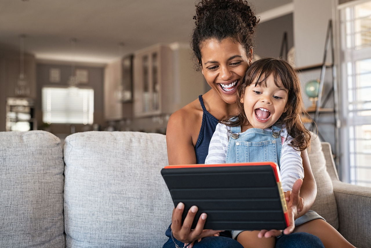 Young mother and smiling daughter playing on digital tablet at home