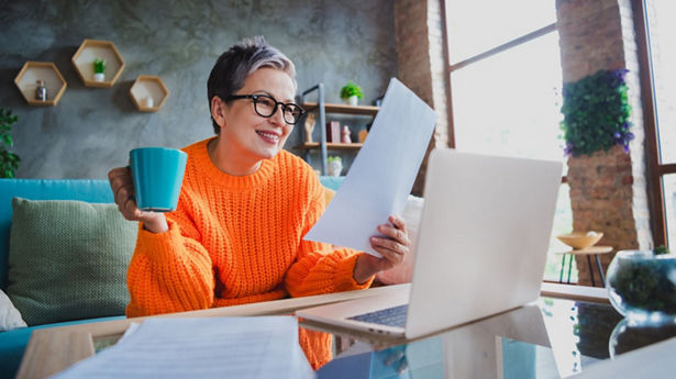 Person holding a turquoise coffee cup while reading a piece of paper at their desk