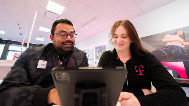 Two T-Mobile employees sit together while looking at a tablet