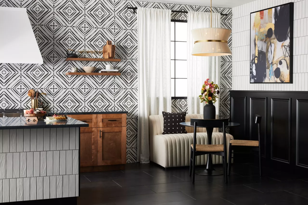 A stylish kitchen and dining area features bold black-and-white geometric tile, warm wood cabinets, a small dining set, and a contemporary cream-colored loveseat.