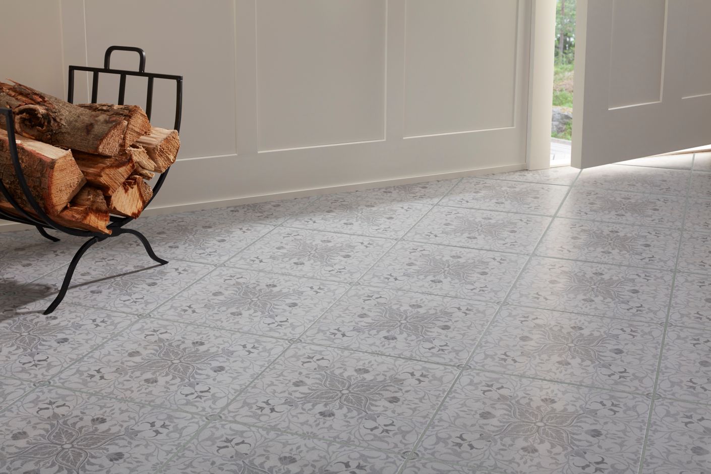 Detail view of home entryway with grey floral patterned floor tile and fireplace log carrier.