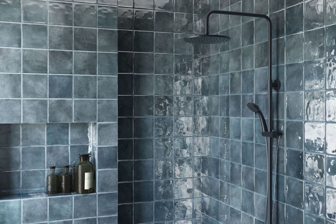 Square blue tiles, made in the style of handmade Moroccan tiles, feature varied shades of medium-to-dark blue and a subtly textured surface. In this bathroom, the tile is used to cover all parts of a shower wall from floor to ceiling, including the recessed shower niche.