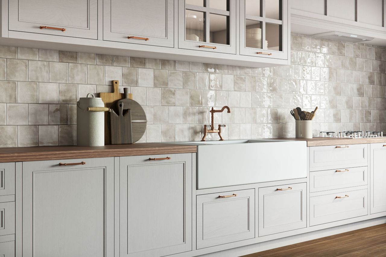 This kitchen features an off-white handmade-look tile backsplash, white cabinets and a farmhouse-style sink.