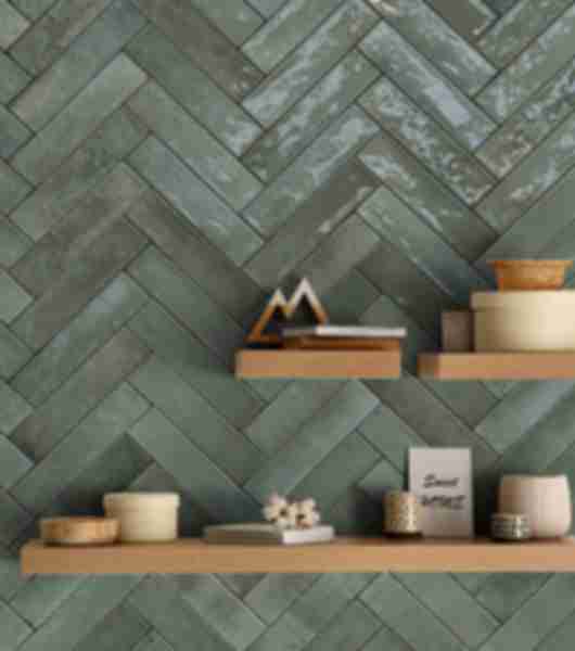 Wall covered in green porcelain subway tiles arranged in a herringbone pattern.