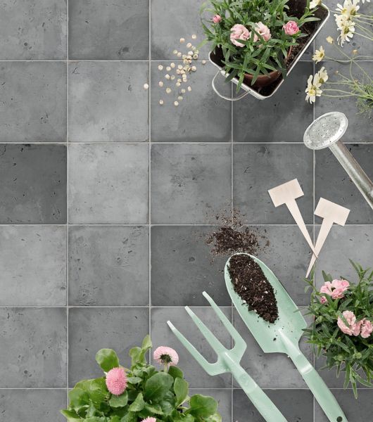 Small square-shaped porcelain patio floor tile in shades of grey. With plants and gardening tools.