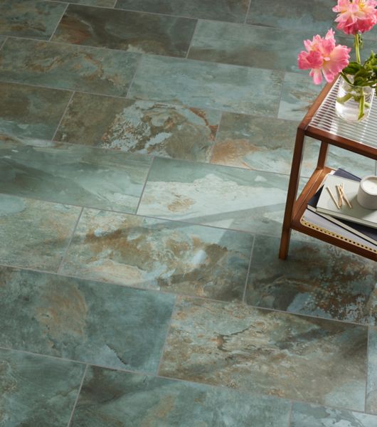 The floor of a living space is covered in large-format porcelain tile in layered shades of green that realistically mimic the appearance of natural slate.