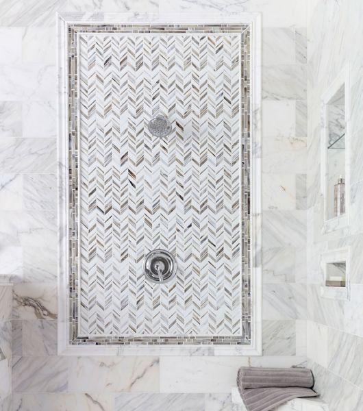 The focal point of this shower is the large accent wall. A glass chevron mosaic (in shades of grey, beige, ivory and black) is installed on the wall behind the shower fixtures and framed by rows of glass linear mosaic tile in complementing colors.