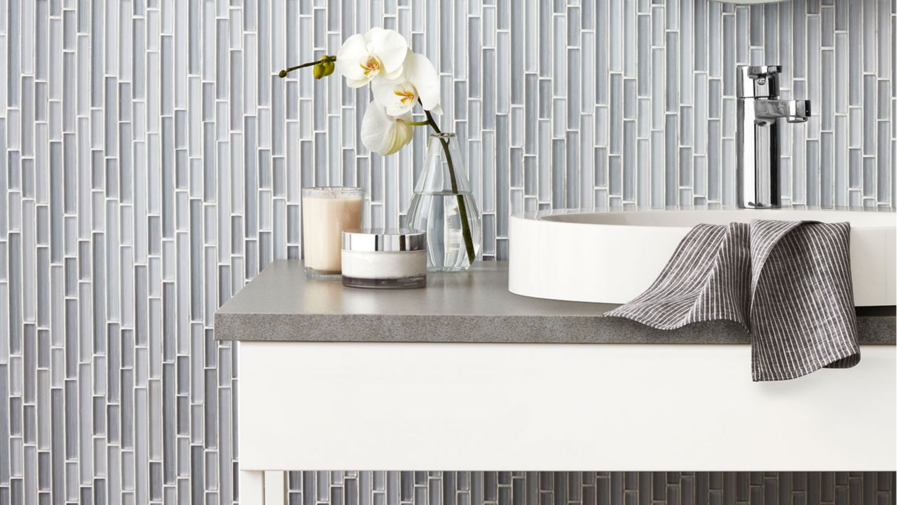 Bathroom vanity with gray and white glass mosaic backsplash tile in a staggered vertical pattern, round sink, chrome faucet, and orchid decor.