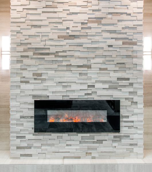 A modern wall-mounted fireplace is mounted on a wall of light grey limestone architectural tile running from floor to ceiling.