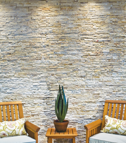 Highly textured travertine architectural tile creates a rustic feel on this outdoor wall. With two chairs and a small table with a plant.