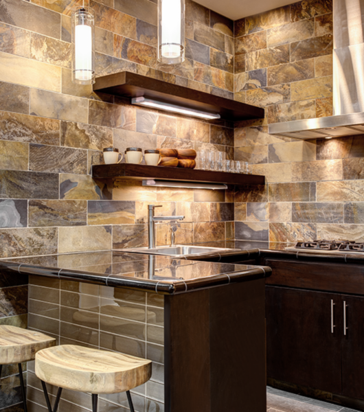 The walls of this kitchen are covered in large, multi-colored slate subway tiles arranged in a traditional brick layout. The slate tiles begin above the counter and extend the full height of the room, up to the ceiling.