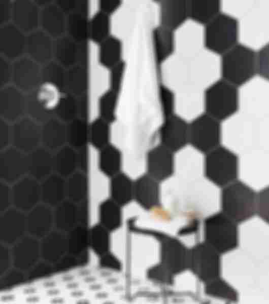 Black porcelain hexagonal tile covers one full shower wall, while the adjacent shower wall and shower floor feature black-and-white mosaic designs of varying sizes.