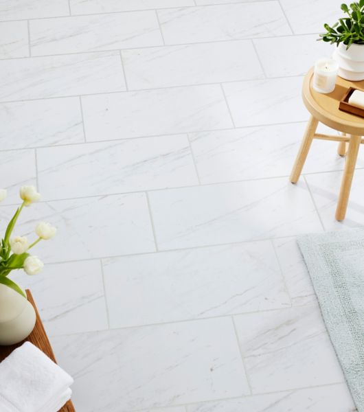 Bathroom floor covered in large-format marble-look porcelain tile. The white tile with delicate gray veining is precisely color-matched to genuine Volakas marble for a highly realistic appearance.