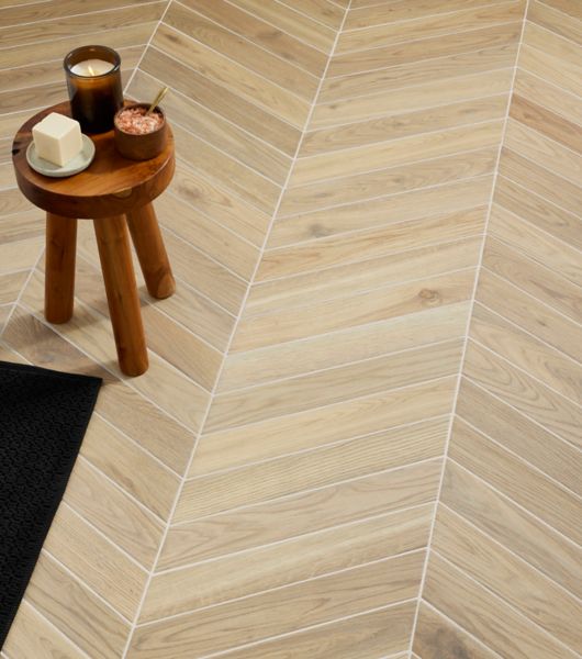 This floor is covered in light-tone, wood-look porcelain tile in chevron shapes arranged in stylish zig-zag rows.