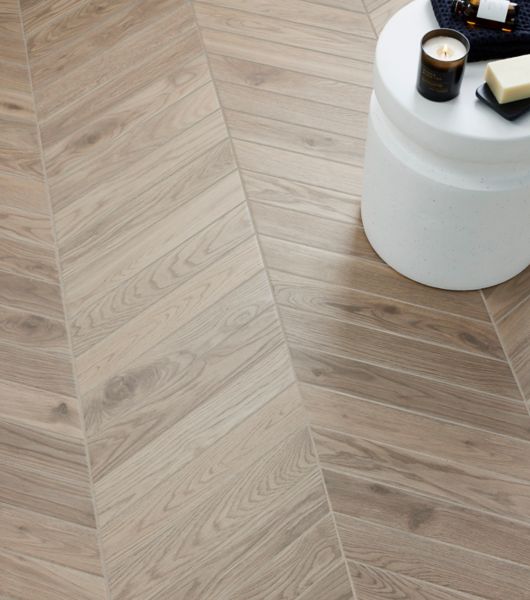 Floor tiled with light brown wood-look chevron tile and a white rounded accent table.