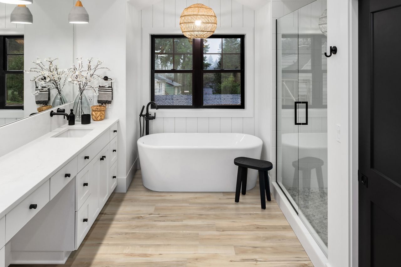 Bathroom with white tub, glass shower doors and wood-look flooring.