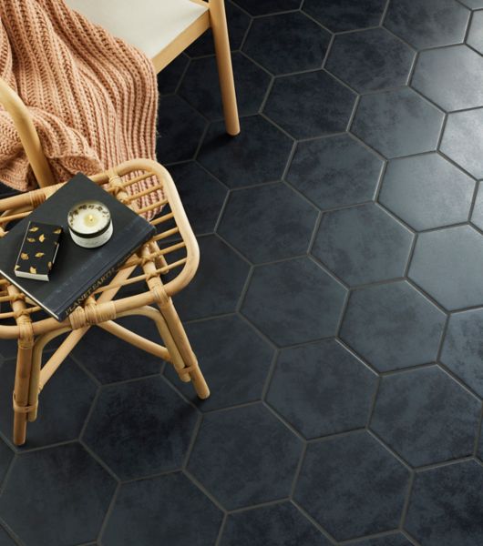 Rattan furniture is arranged in a space with a floor covered in dark hexagonal porcelain tiles.