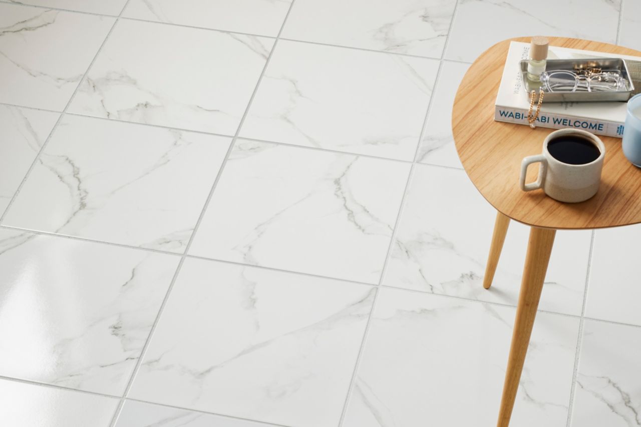 The floor of this living space features square ceramic stone-look tiles. They have the appearance of white marble with light gray veining, and a polished finish.