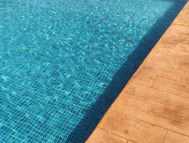A pool with blue tile and wood-look patio tile.