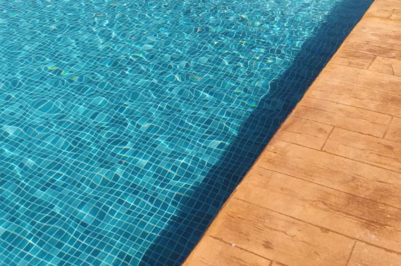 A pool with blue tile and wood-look patio tile.