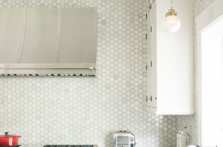 Silver stove with red nobs in front of white hexagon tile wall