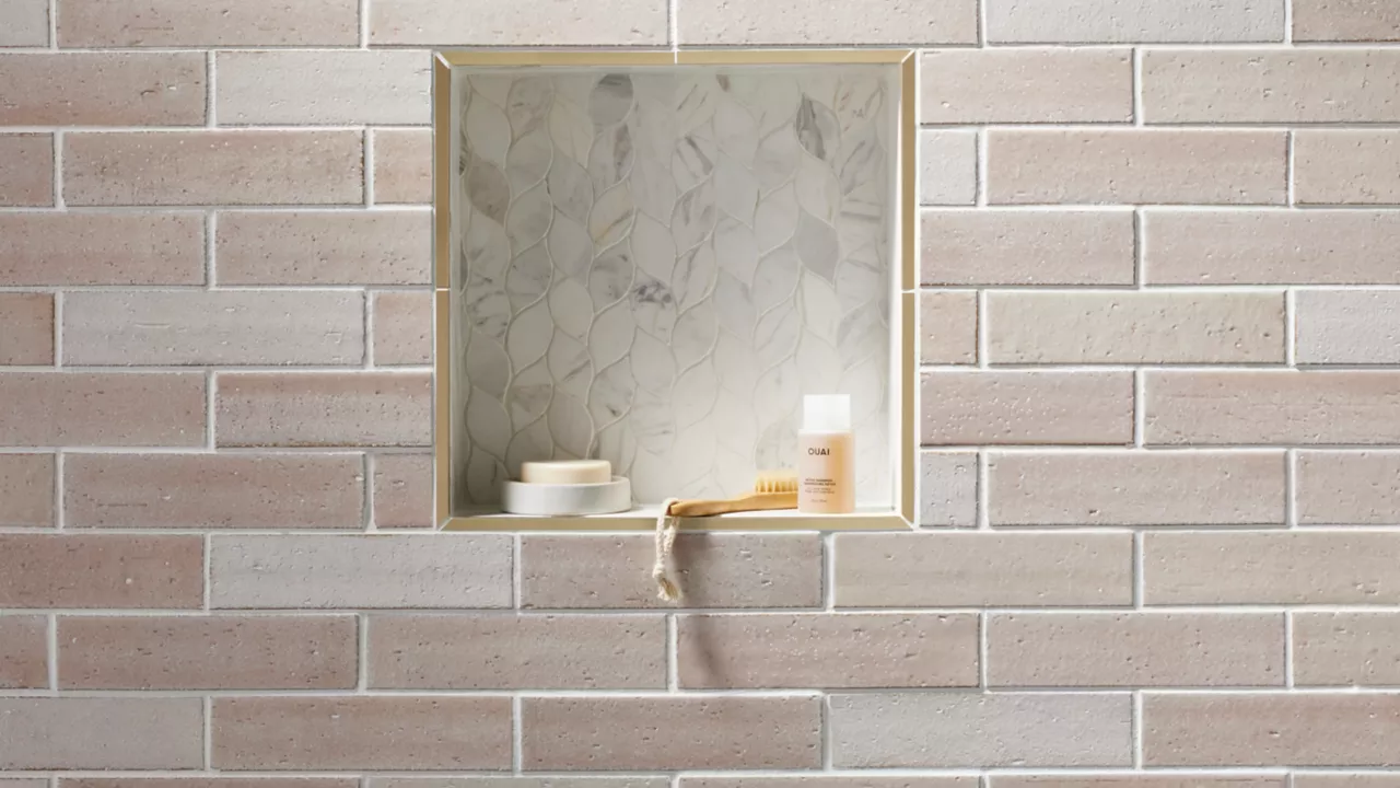 Blush-colored brick-look subway tile with marble leaf-shaped shower niche.
